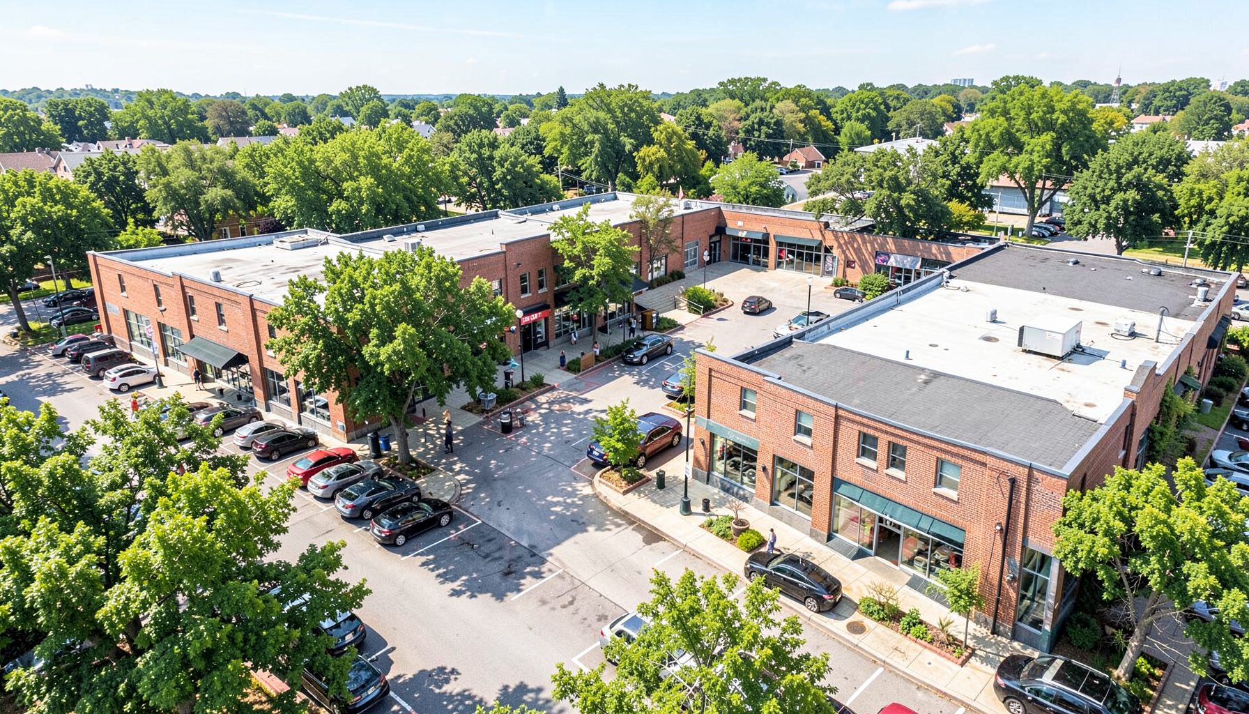 Aerial view of a walkable shopping center with brick buildings, mature trees, and parked cars on a sunny afternoon