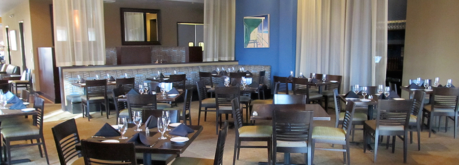 Restaurant dining area with dark wood tables, set with glassware and napkins, blue accent wall